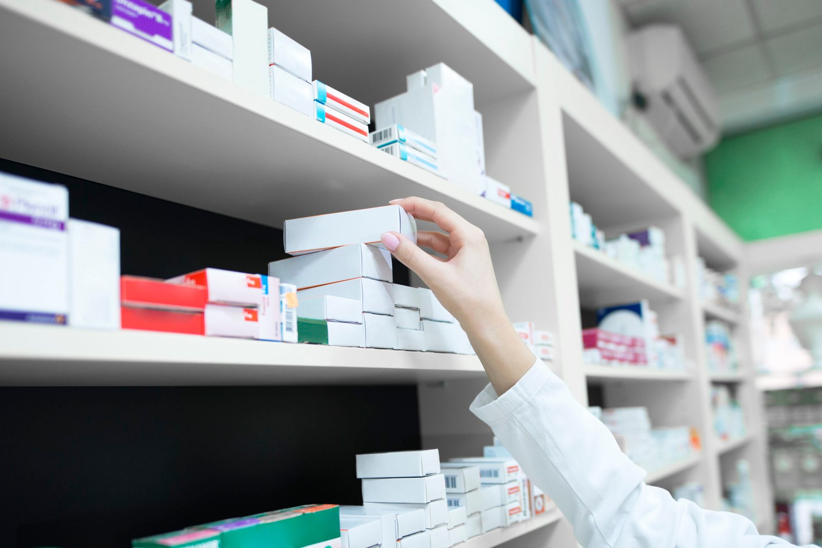A pharmacist’s hand selecting a medicine box from a pharmacy shelf