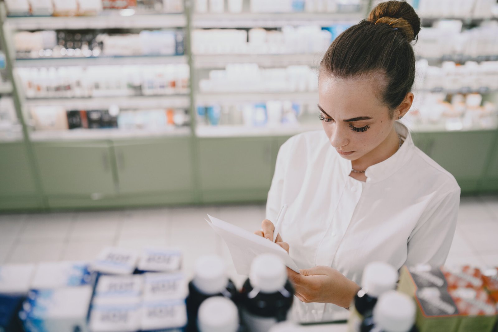 A pharmacist reviewing paperwork beside shelves of medicines