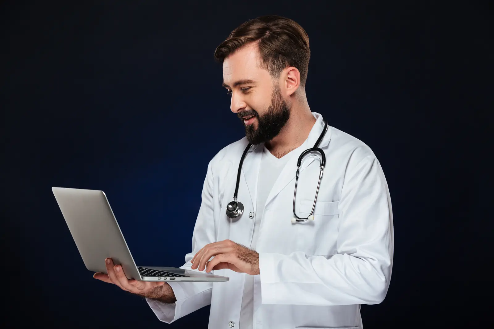Doctor holding an open laptop and looking at its screen.