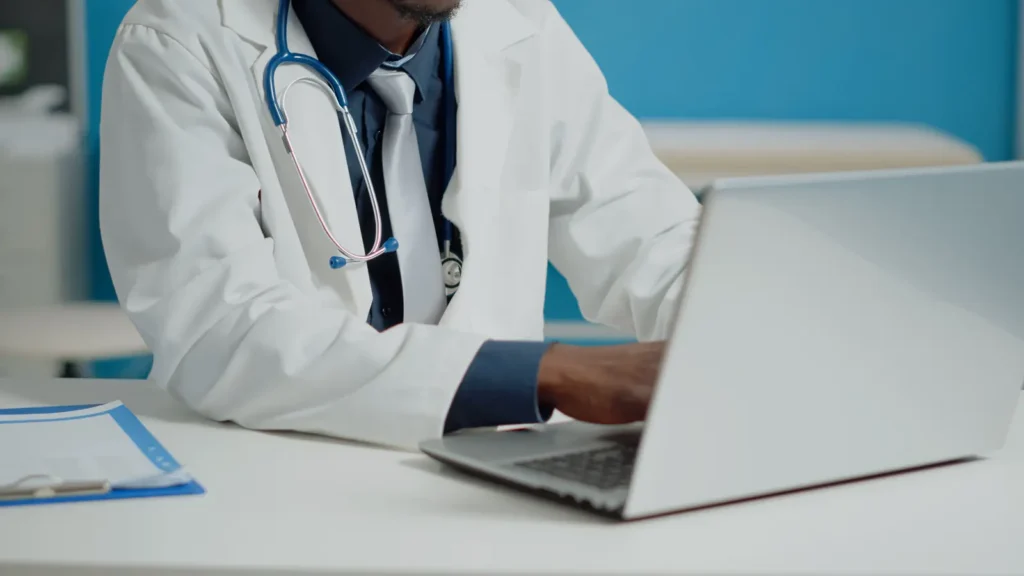 Doctor typing on a laptop at a medical office desk.